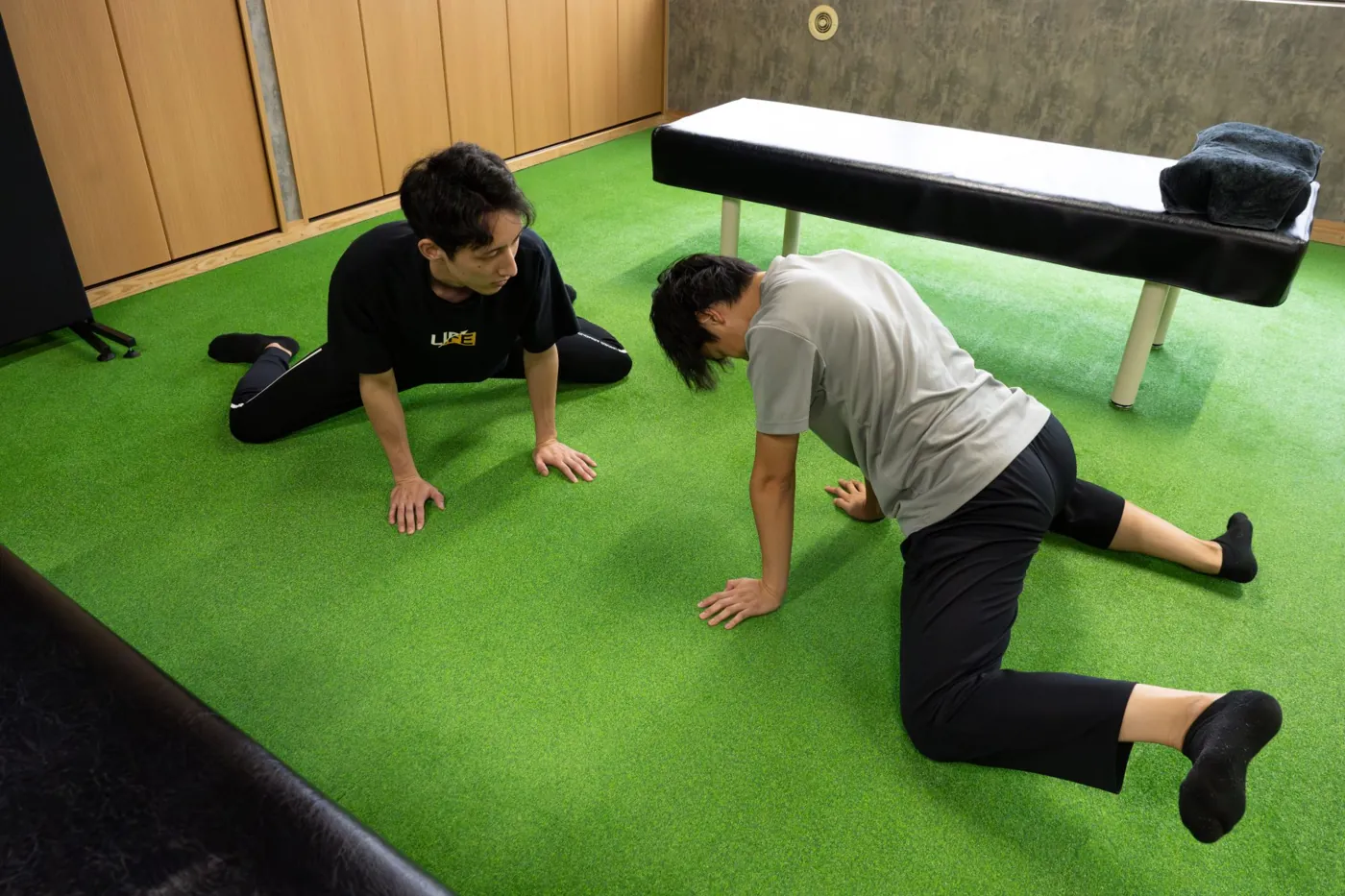 人工芝の上で、トレーナーがお手本を見せながらセルフストレッチを指導している様子